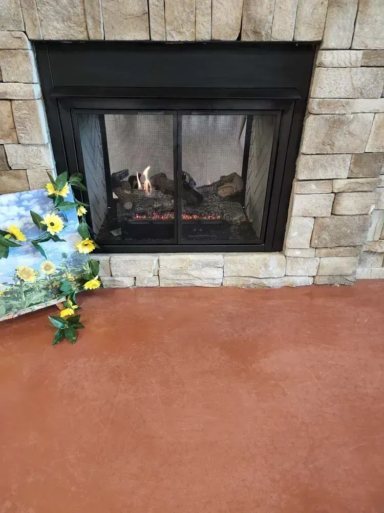 Fireplace with burning logs, encased in stone, with a painting of sunflowers to the left.
