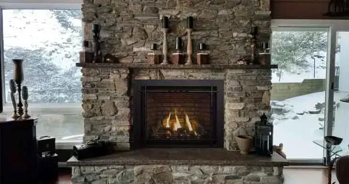 Stone fireplace with fire burning, mantle with candles, flanked by windows showing snowy landscape.