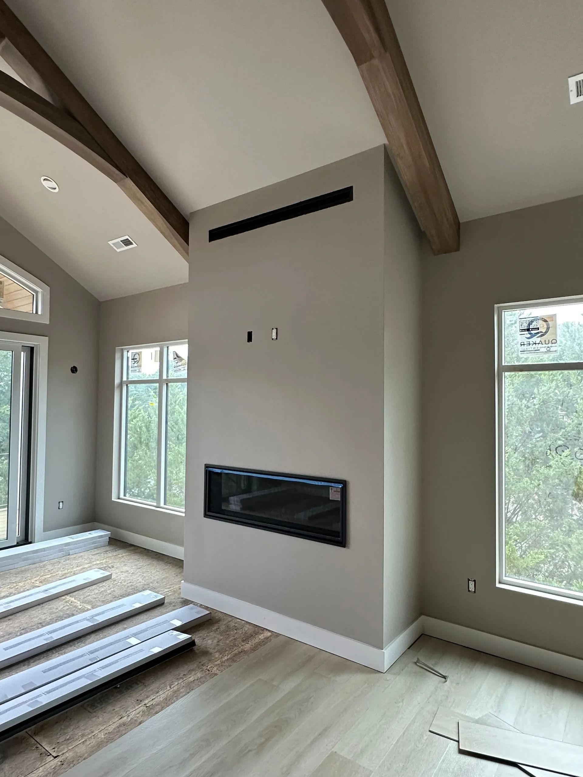 Living room with fireplace, windows, light wood floors, beige walls, and wood beams.