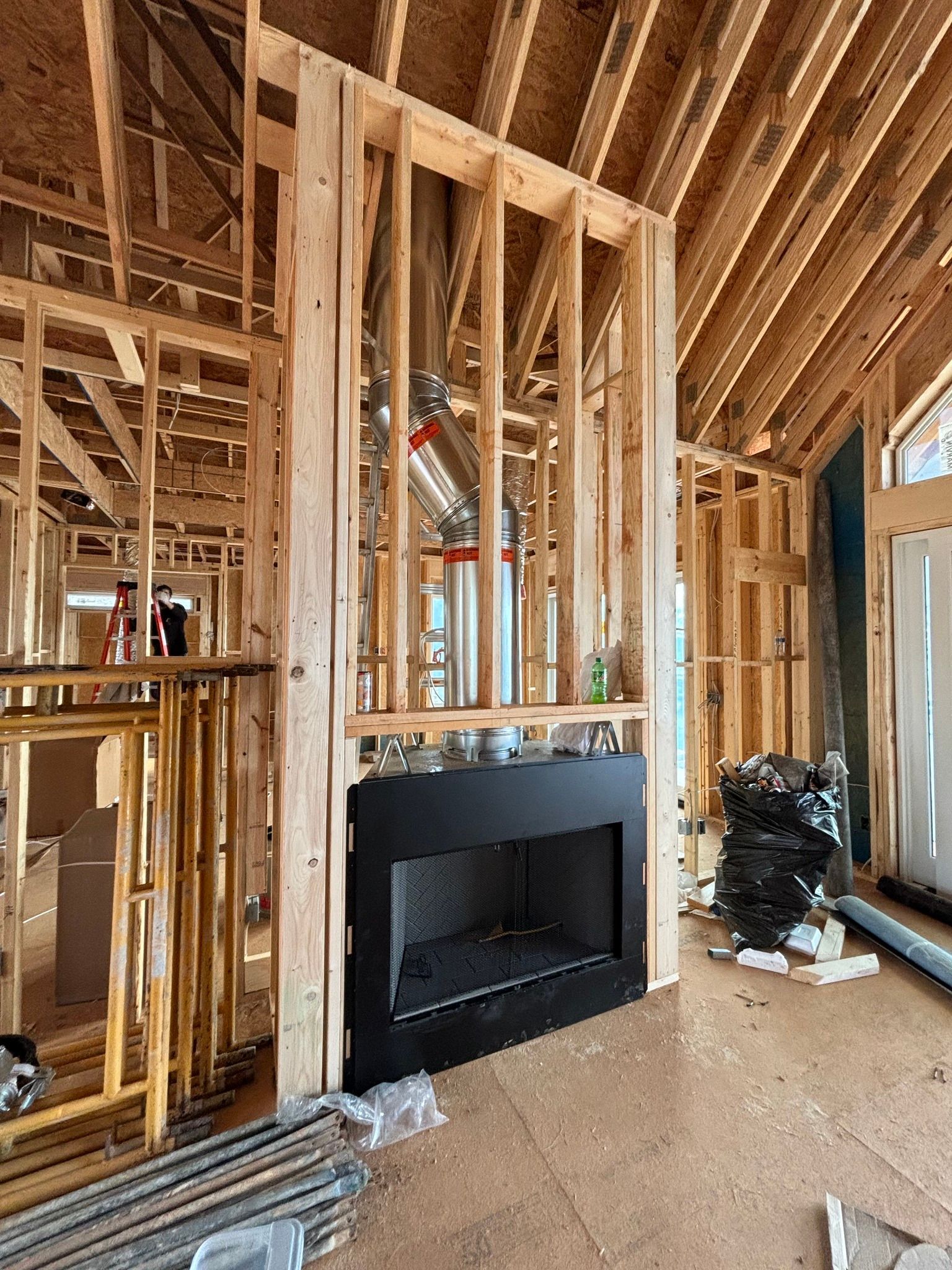 Interior of a house under construction; a black fireplace is framed by wooden studs with ductwork visible.