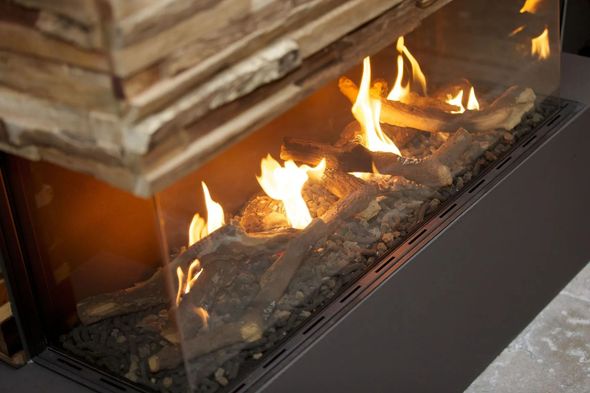 Fireplace with flames and faux logs behind glass panels, with stone detail on top.
