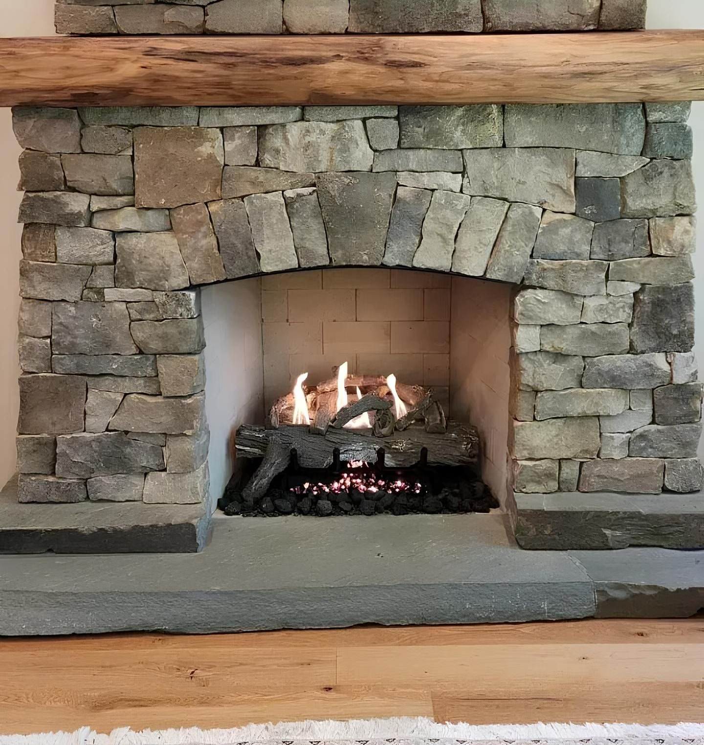 Stone fireplace with a burning gas fire, wood beam mantel, and mounted TV.