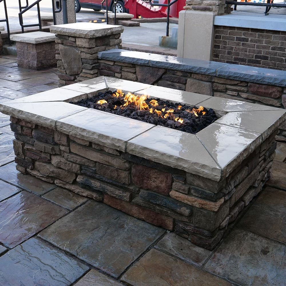 Stone fire pit with flames, on a stone patio, with benches.