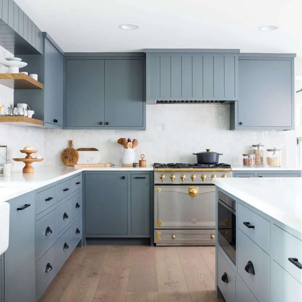 Blue-gray kitchen with gold accents, white countertops, and a stainless steel stove in a bright modern room
