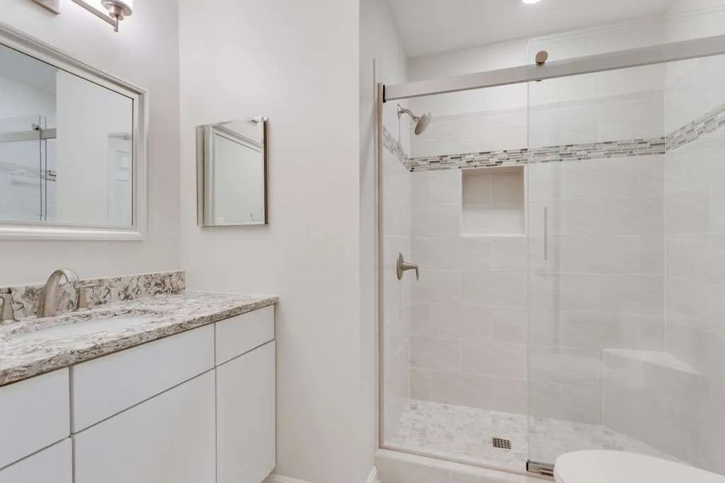 Bright white bathroom with marble vanity, wall mirror, and glass shower enclosure