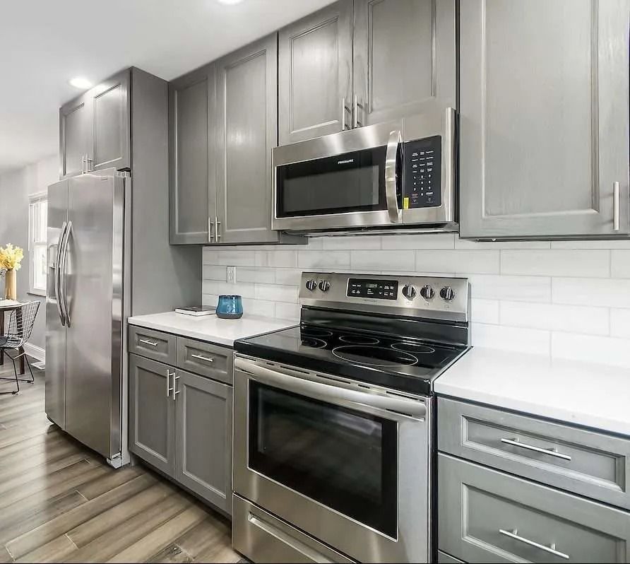 Modern kitchen with stainless steel appliances, gray cabinets, white subway tile, and wood flooring