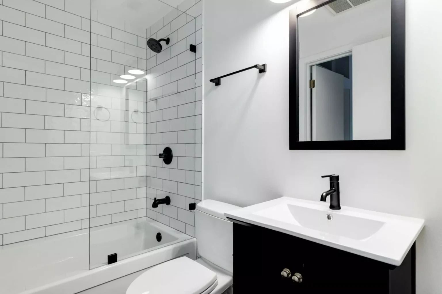 Modern white bathroom with glass shower, vanity sink, and black accents