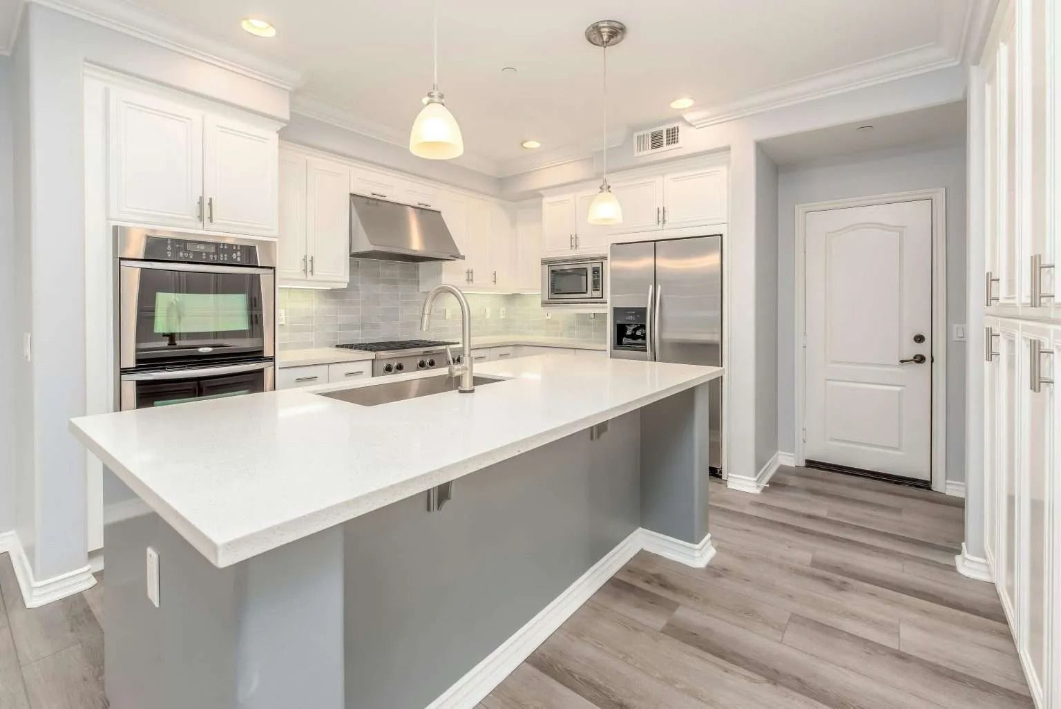 Bright modern kitchen with white cabinets, stainless appliances, large island, and gray wood floors