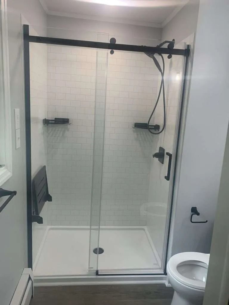Glass walk-in shower with black hardware and a wall-mounted seat beside a toilet.