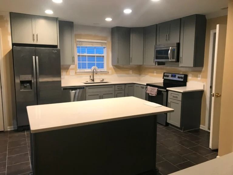 Modern kitchen with dark cabinets, stainless steel appliances, white island, and tiled floor