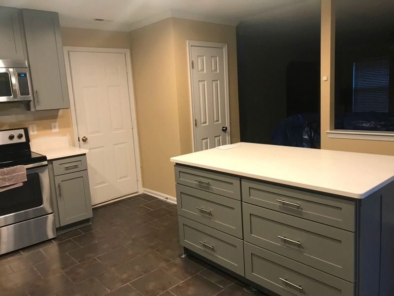 Kitchen with gray cabinets, stainless stove, and a large white island on dark tile floor.