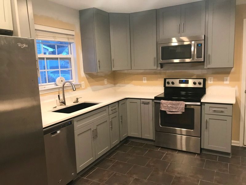 Modern gray kitchen with stainless steel appliances, dark tile floor, and a window over the sink