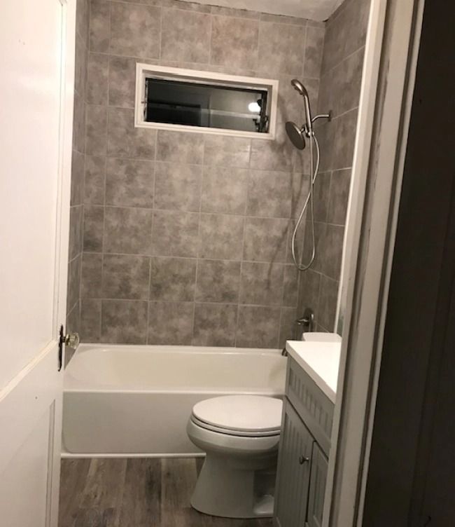 Small bathroom with gray-tiled shower over tub, toilet, and frosted window.