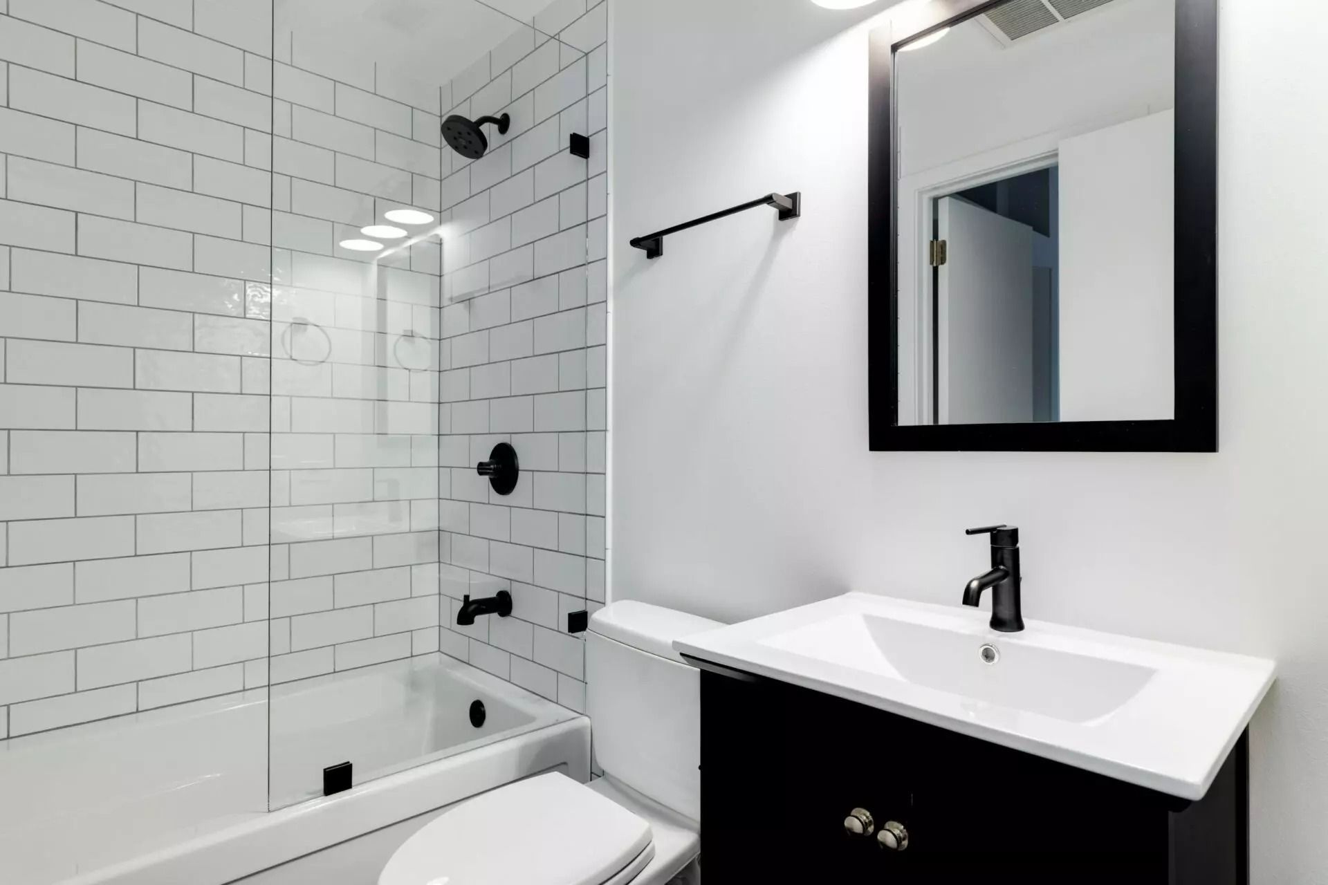 Modern white bathroom with subway tile, bathtub, black fixtures, and a vanity mirror
