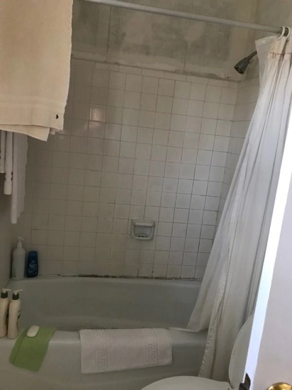 Small bathroom with a tiled shower/tub, white curtain, and toiletries on the ledge.