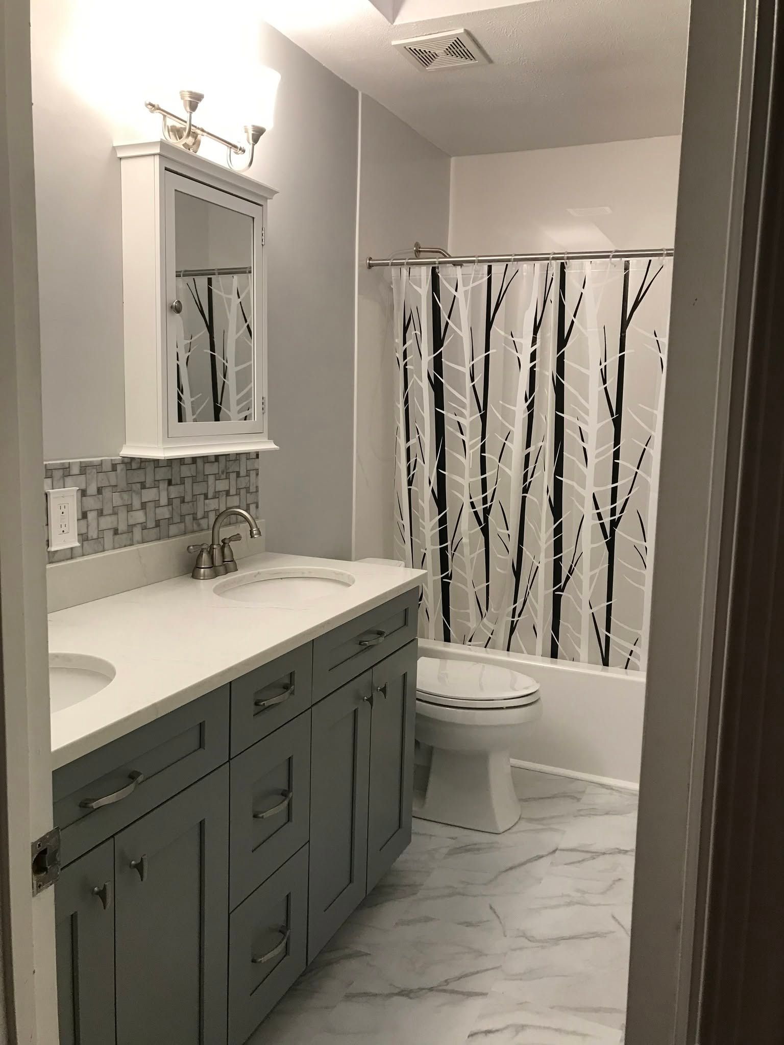 Small bathroom with gray vanity, white sink, patterned shower curtain, and marble-look floor.