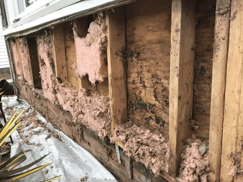 Damaged house wall with exposed studs and crumbling pink insulation during renovation