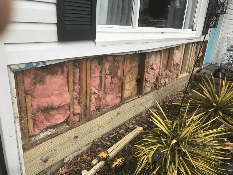 House exterior with damaged wall exposing pink insulation beneath the siding near a window.