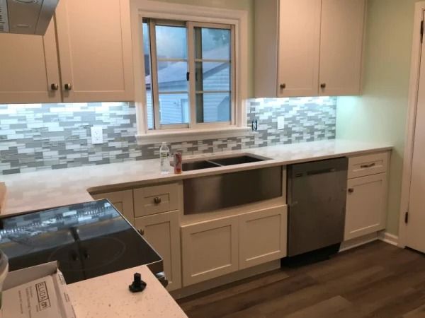 Modern kitchen with white cabinets, mosaic backsplash, stainless sink and dishwasher under a window