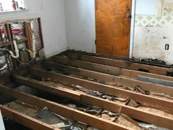 Partially demolished room with exposed floor joists and a wooden door in the background