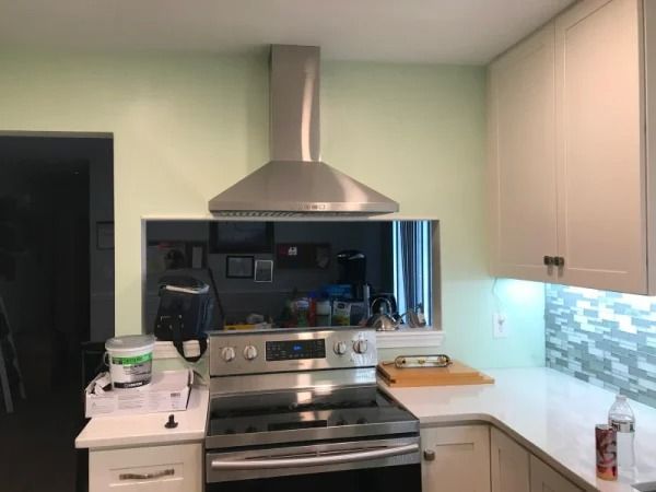 Modern kitchen with stainless steel stove, range hood, white cabinets, and tiled backsplash.