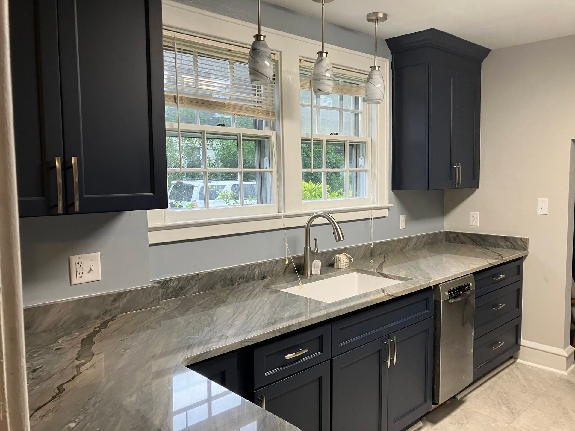 Modern kitchen with dark cabinets, gray marble countertops, and a double sink under a window