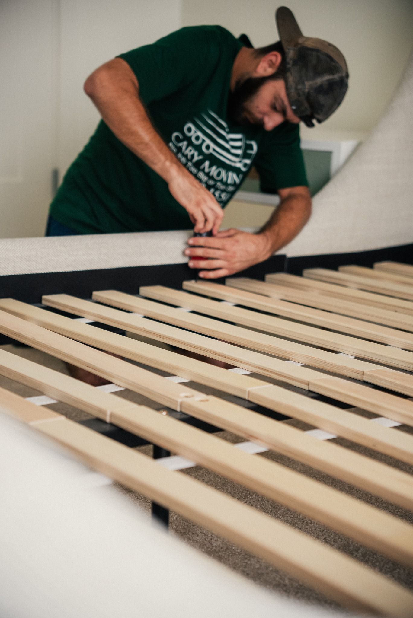 A man in a green shirt is working on a bed frame.