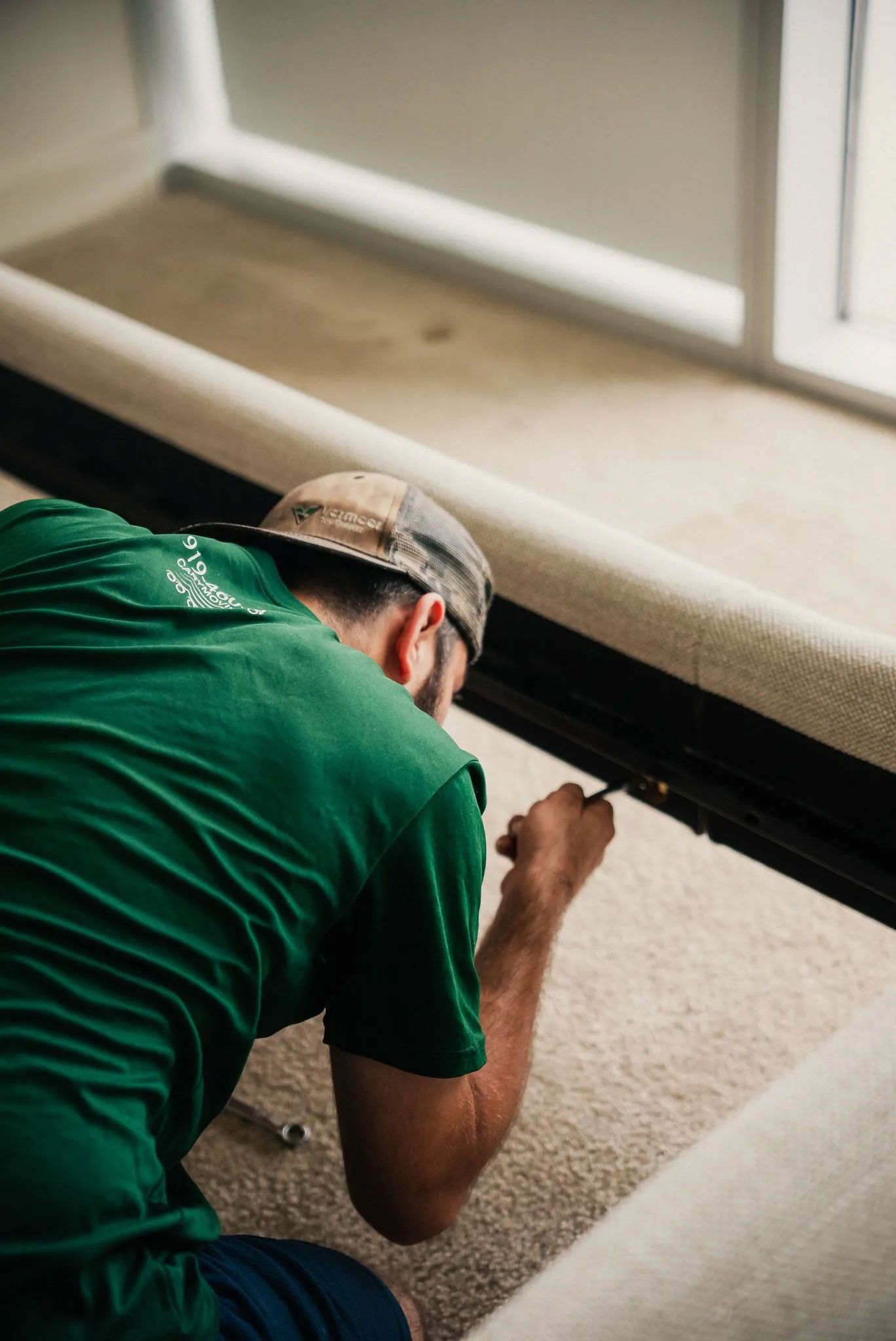 A man in a green shirt is working on a carpet.