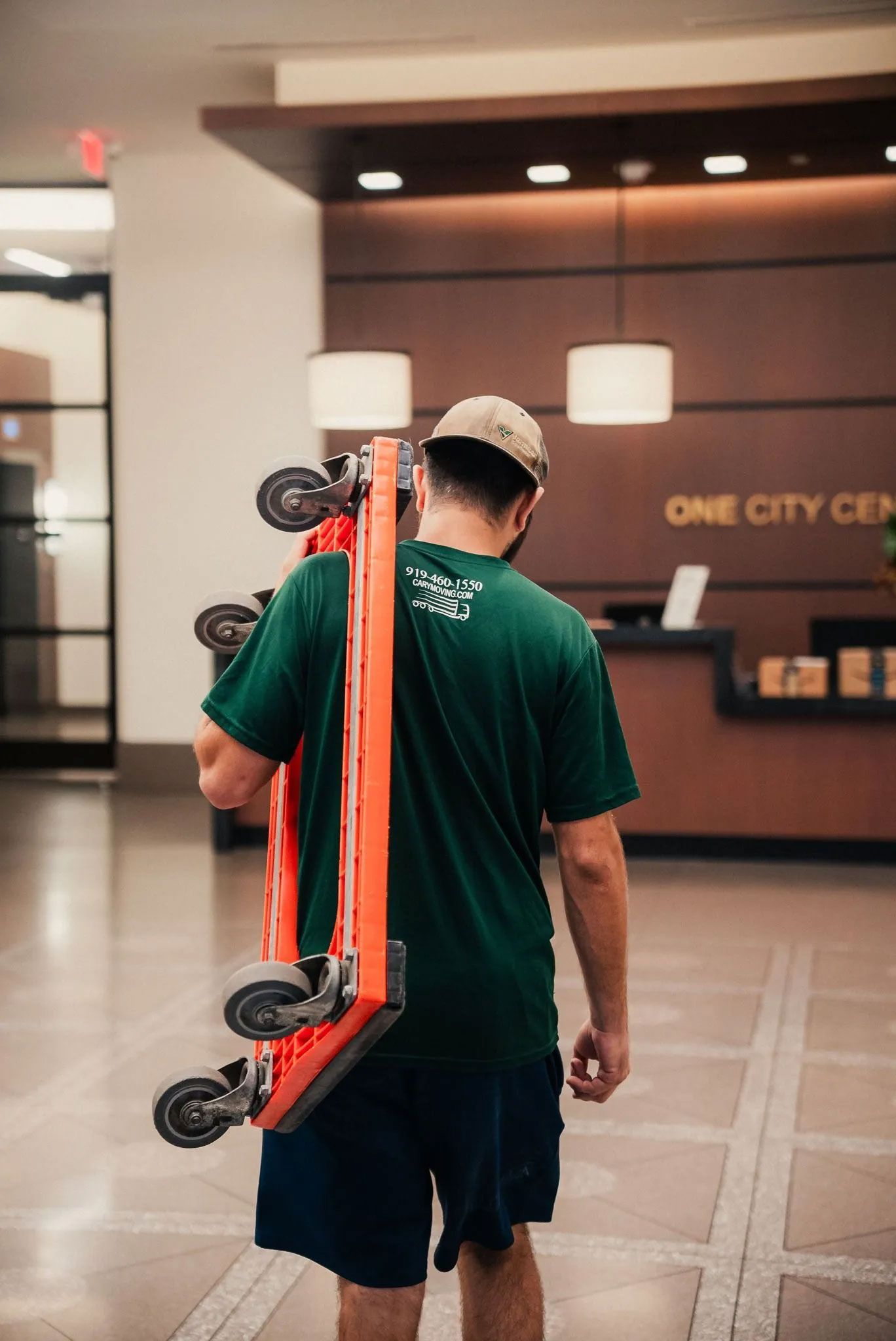 A man is carrying a cart on his back in a lobby.