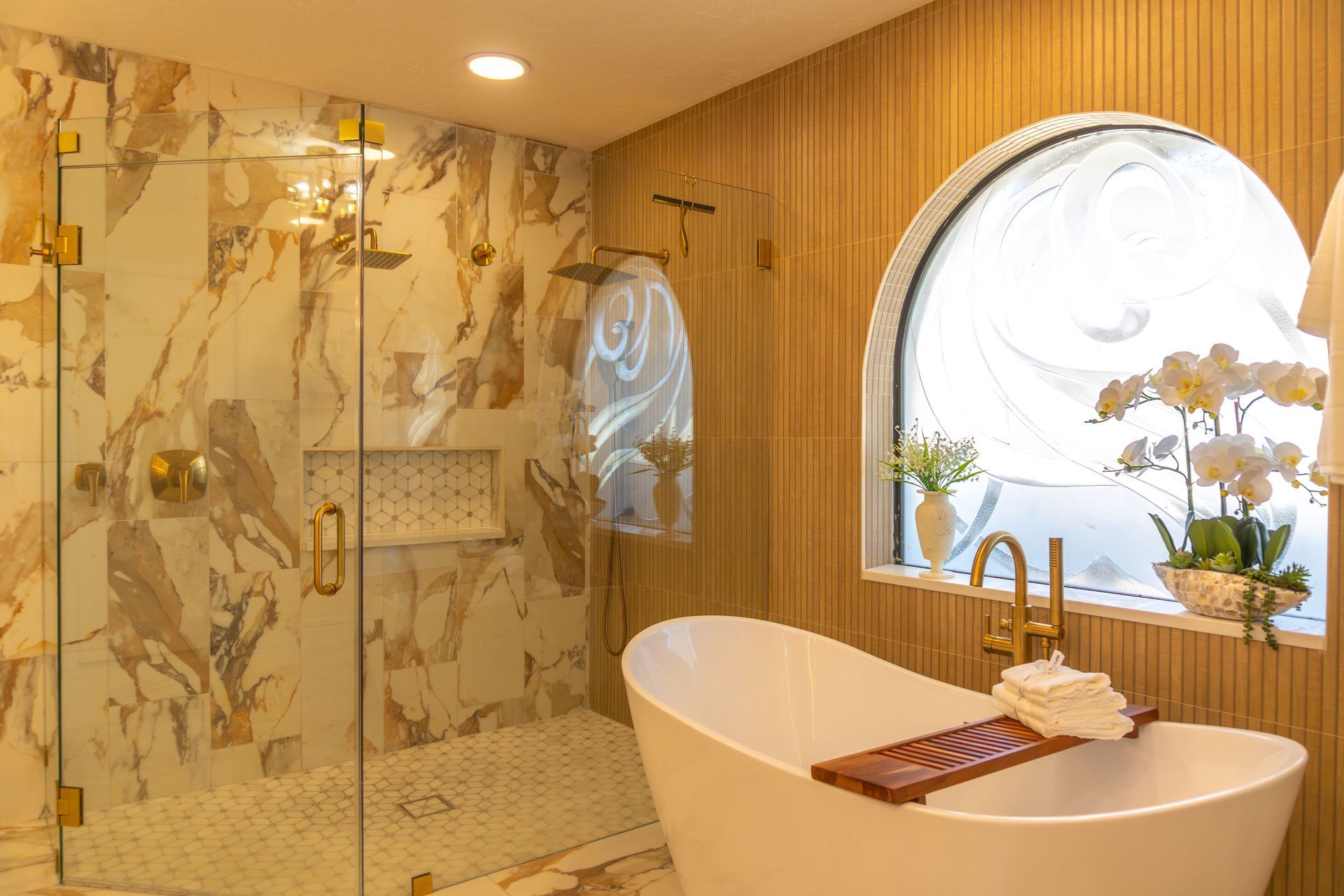 Luxurious bathroom with soaking tub, glass shower, marble walls, and arched window.