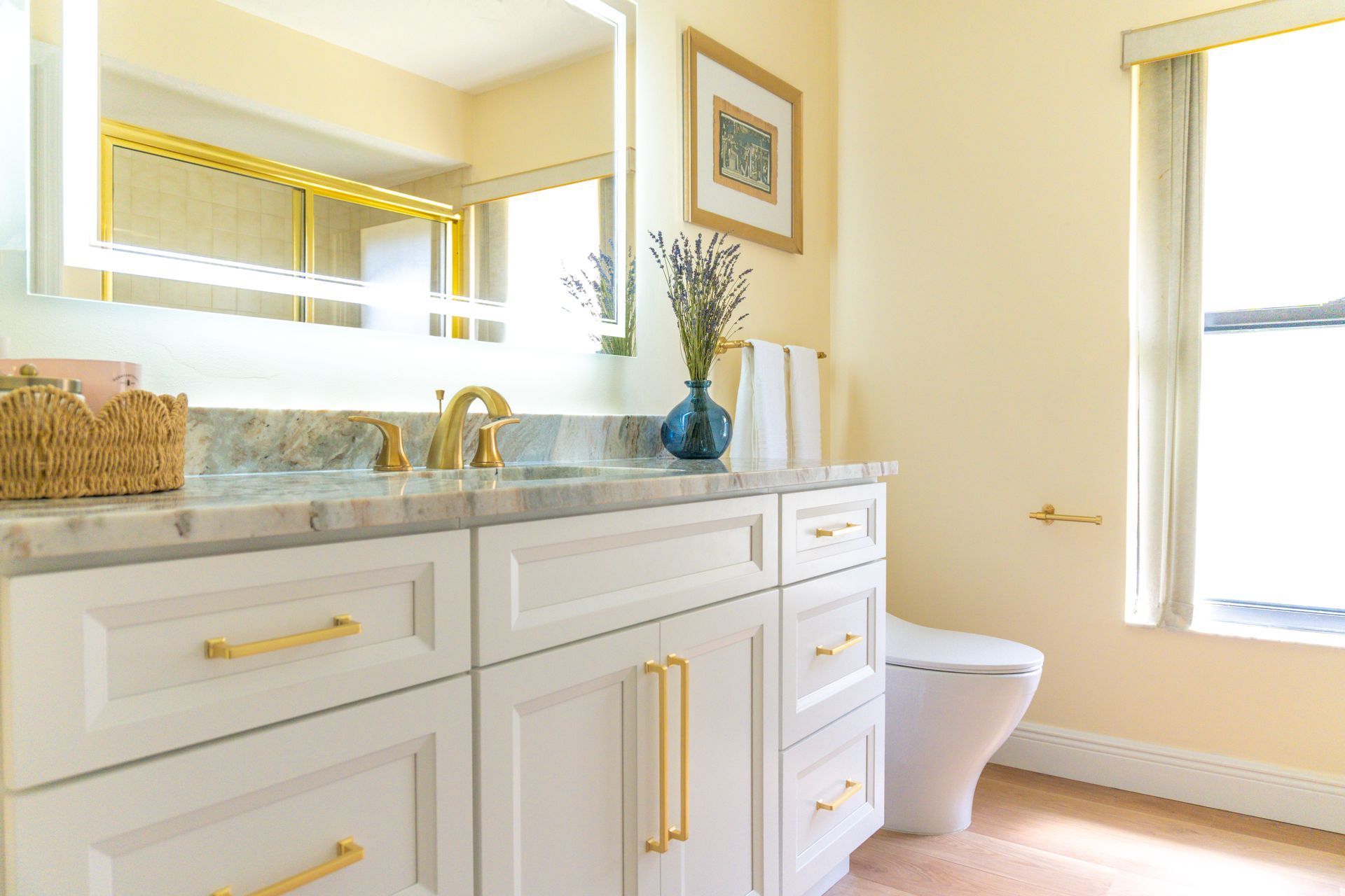 Bathroom with white vanity, marble countertop, gold hardware, and a vase of flowers.