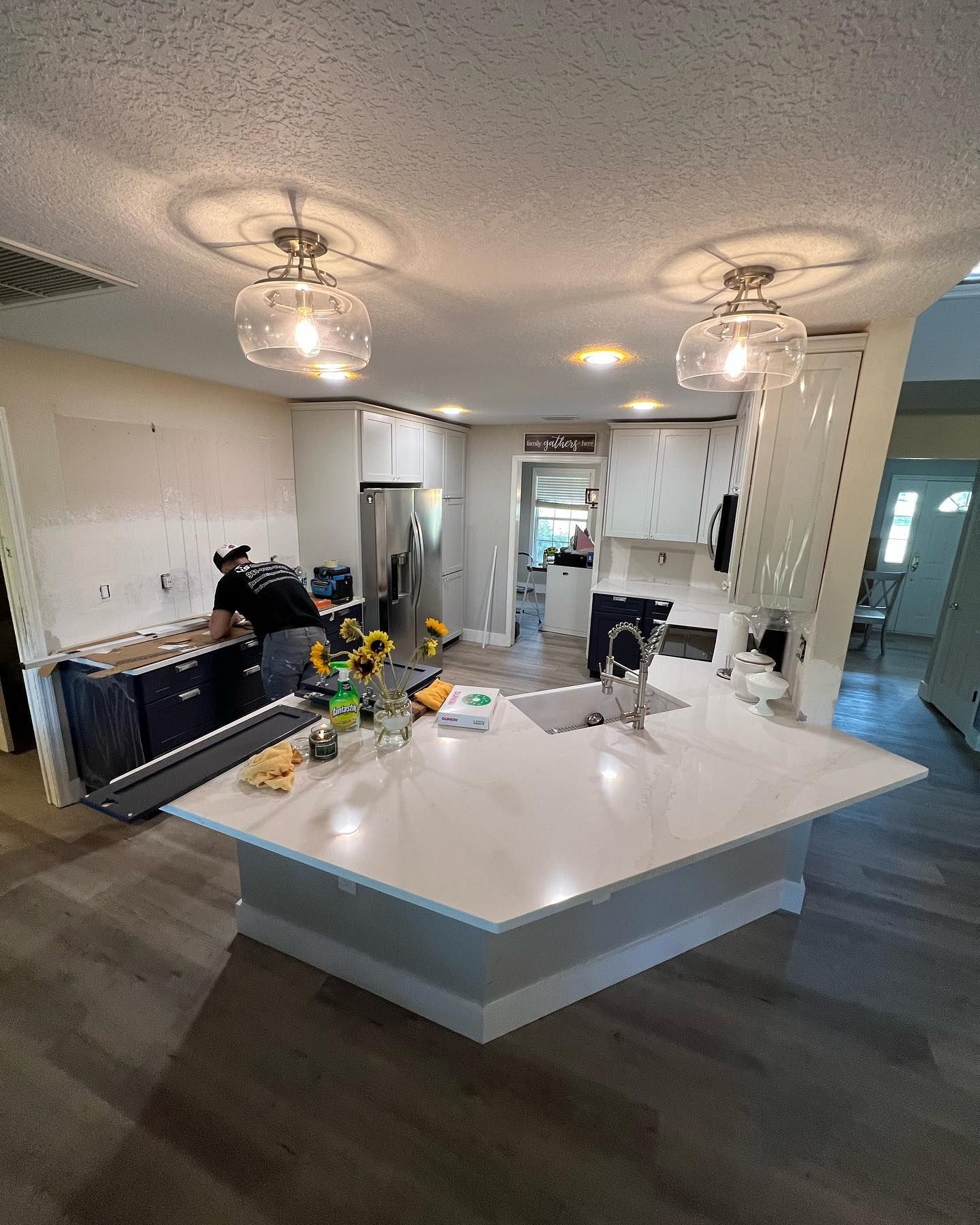 Kitchen remodel in progress: Worker installing cabinets, island with white countertop, new light fixtures.
