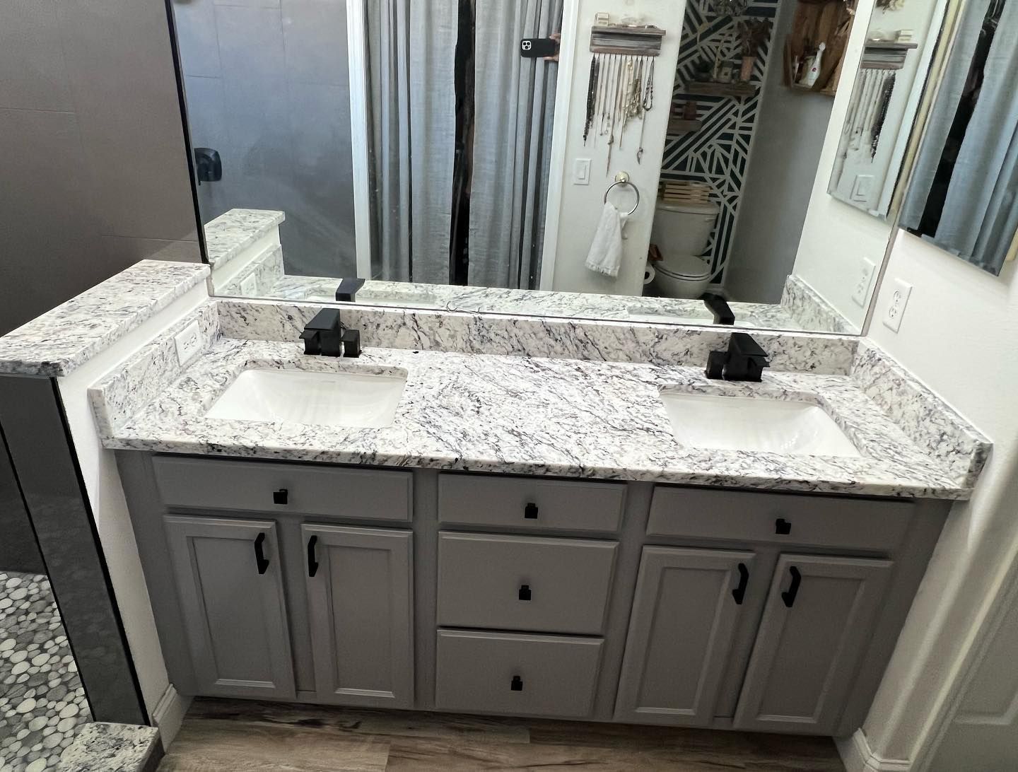Gray double vanity with granite countertop, black fixtures, and gray cabinets in a bathroom.