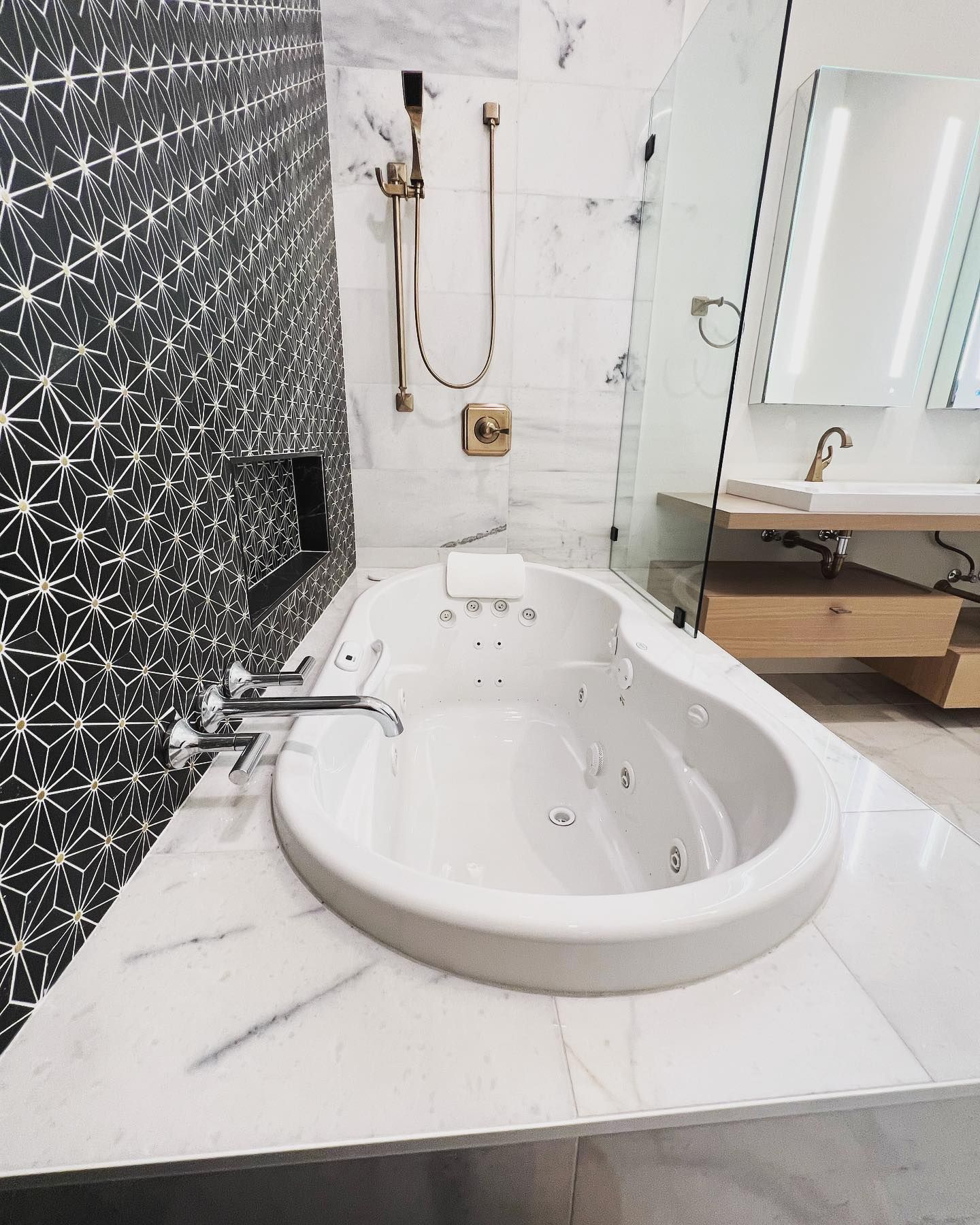 White jacuzzi bathtub in a modern bathroom with gold fixtures and black and white patterned wall.