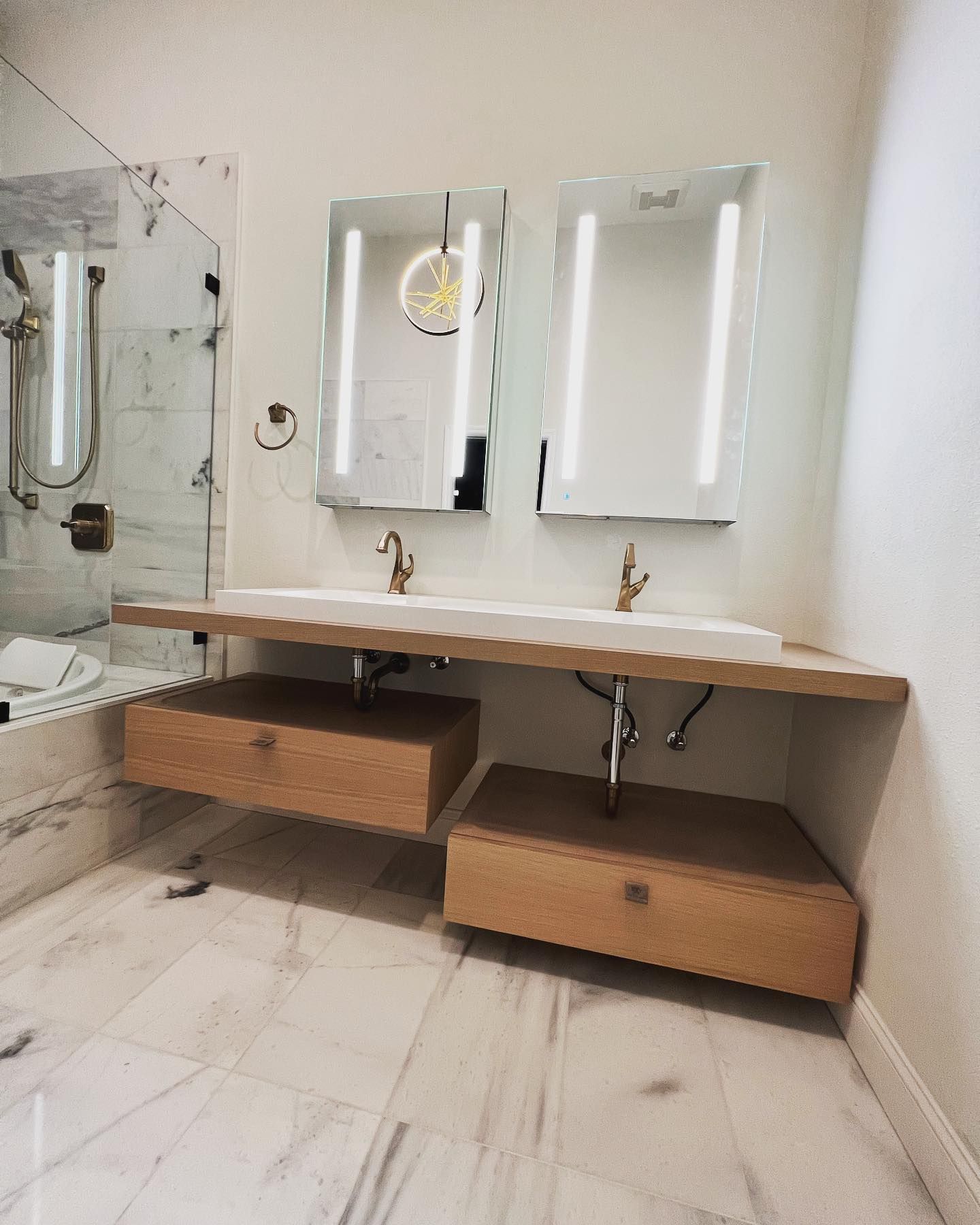 Modern bathroom with floating wooden vanity, two sinks, and two lighted mirrors.