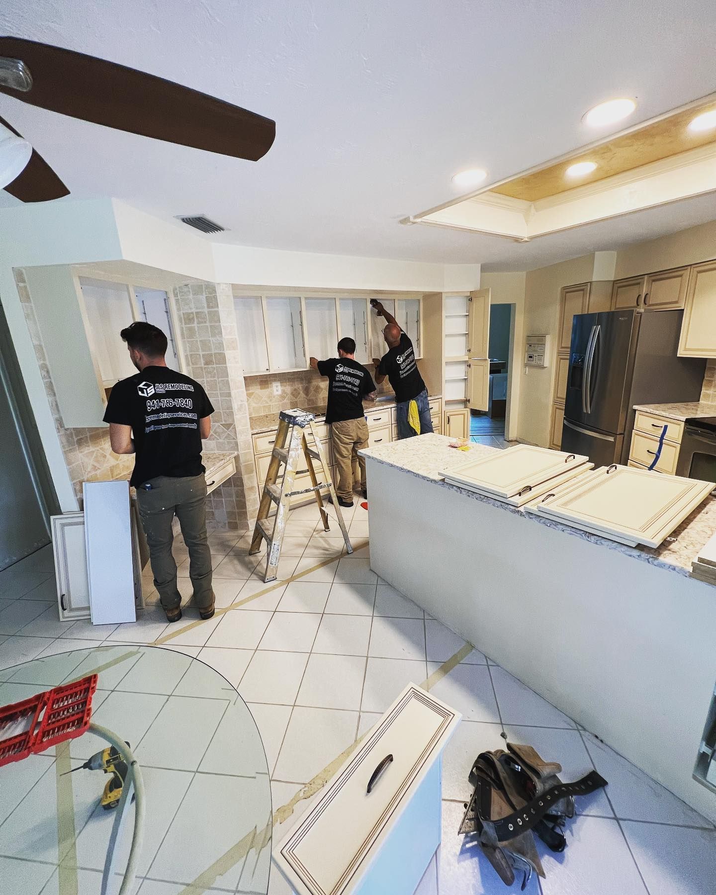 Three workers installing kitchen cabinets. White cabinets, beige walls, white island.