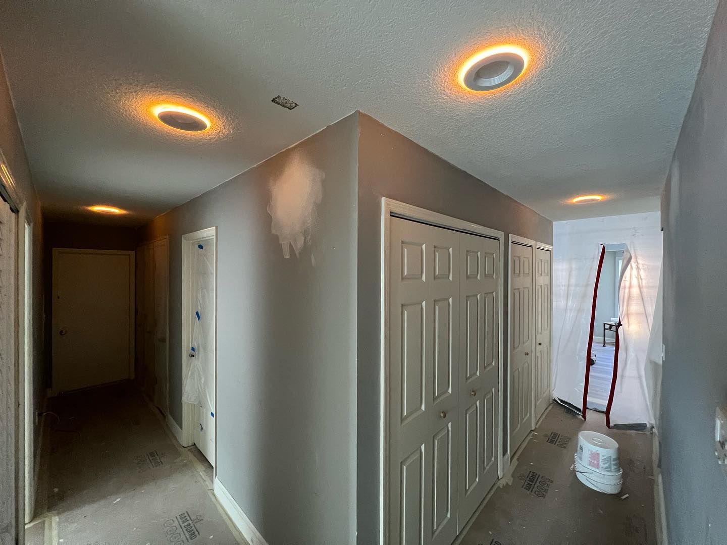 Gray hallway with recessed lighting and closet doors; a person's painting project in progress.