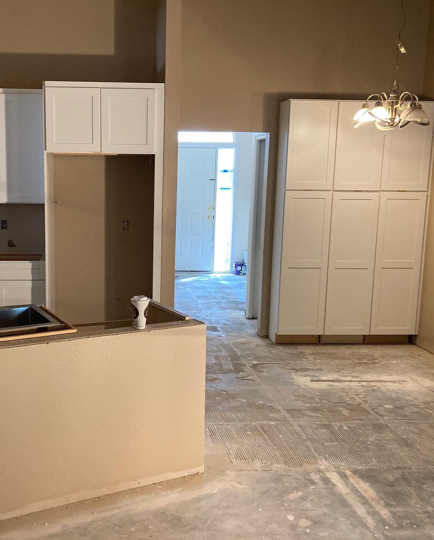 Kitchen under renovation, featuring white cabinets, tan walls, and a view into another room.