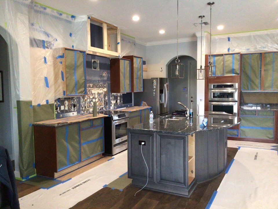 Kitchen under renovation; dark cabinets, island, stainless steel appliances, covered in plastic, blue tape.