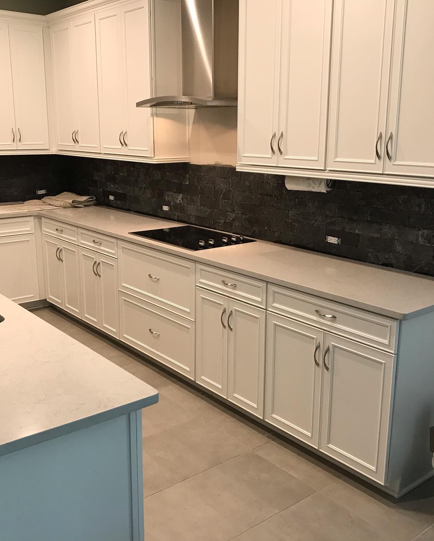 White kitchen cabinets with light countertops and dark backsplash.