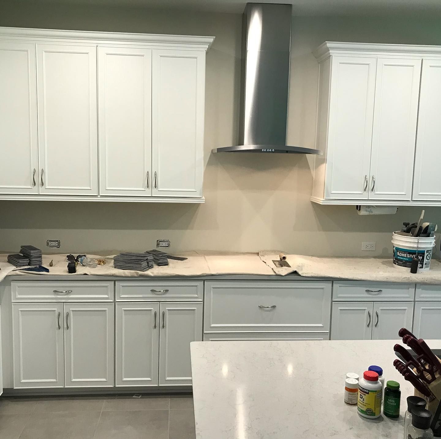 White kitchen cabinets with stainless steel range hood, countertop and island.