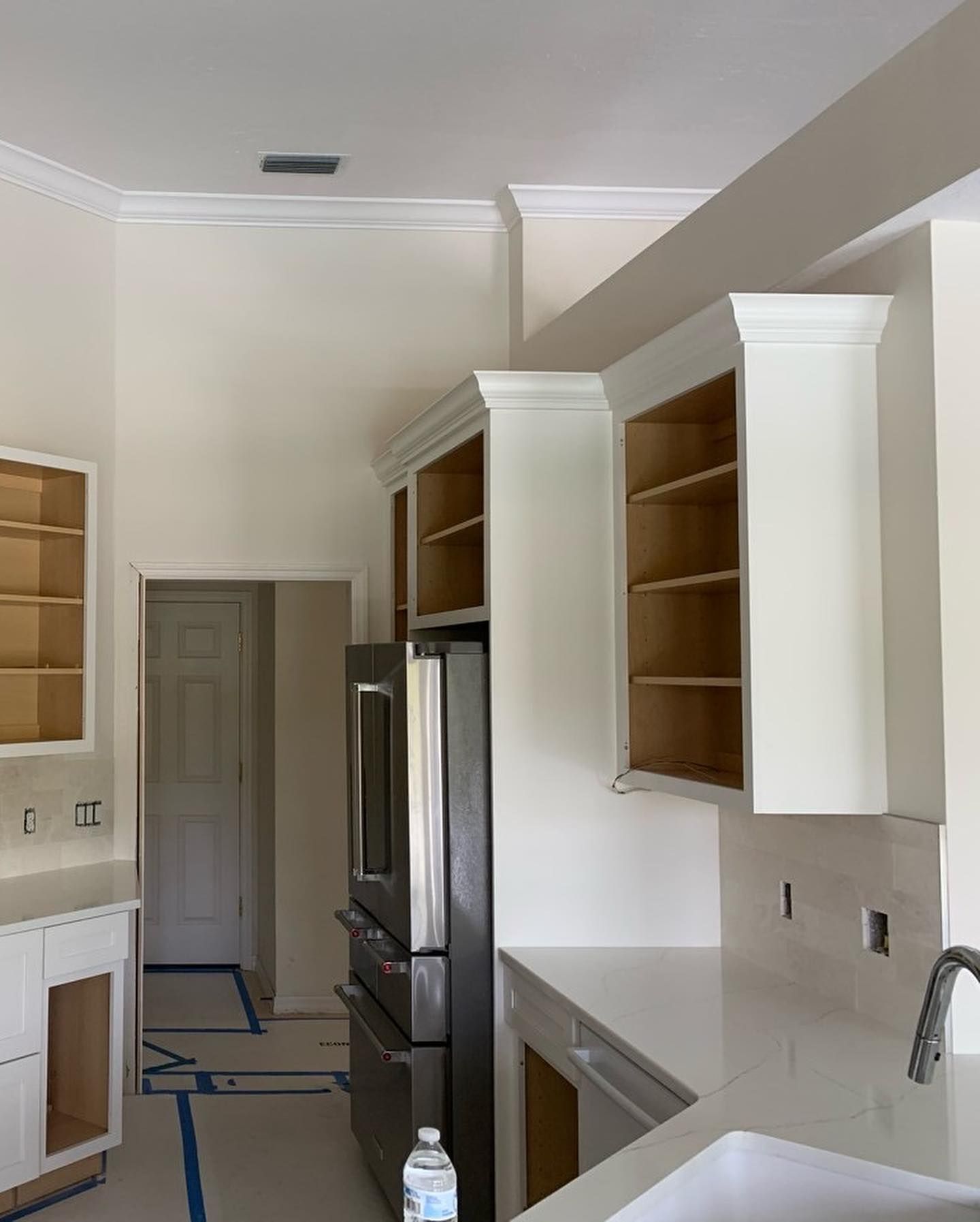 A kitchen under construction with white cabinets, stainless steel appliances, and a tall ceiling.