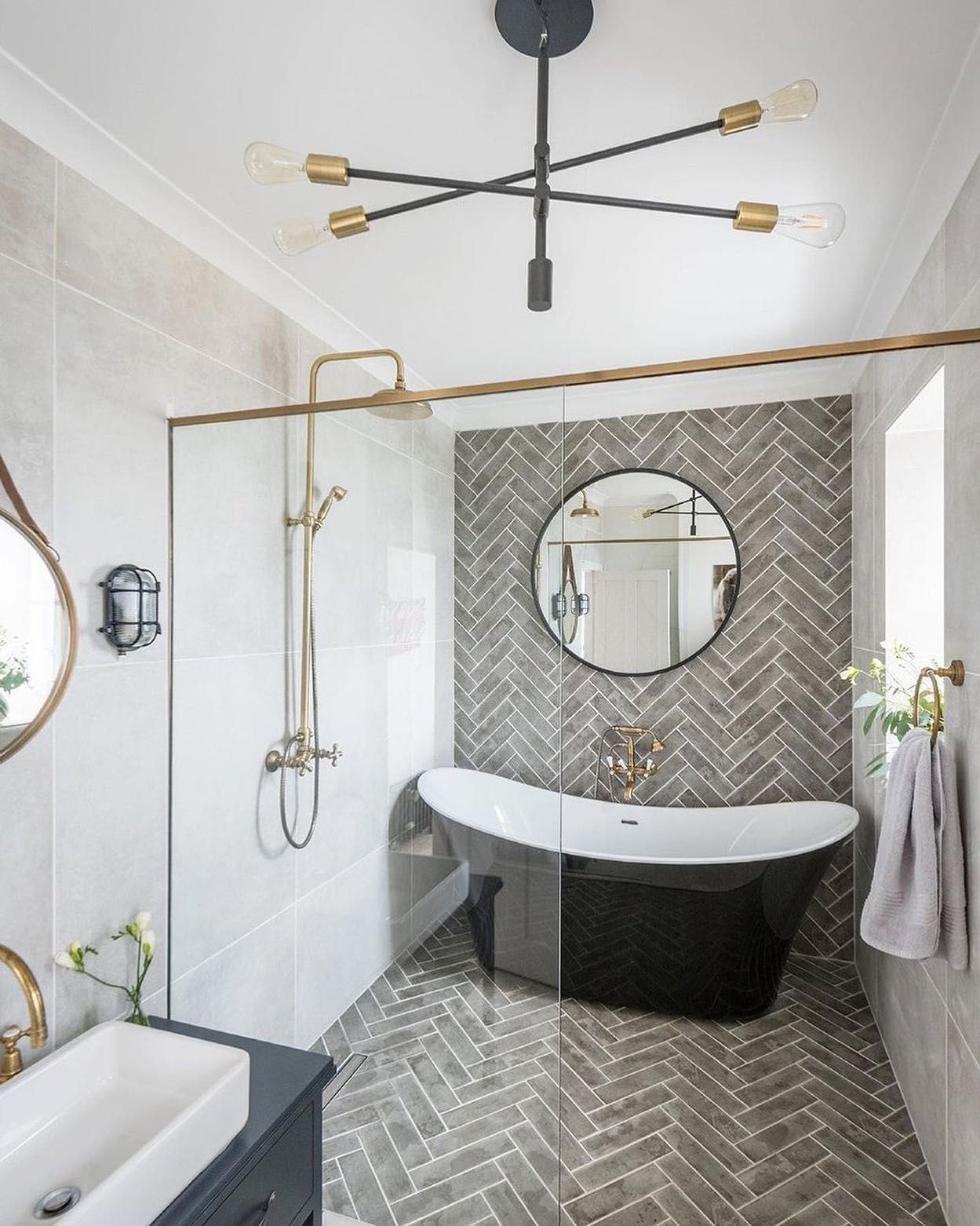 Bathroom with a black bathtub, patterned gray tile, and gold fixtures.