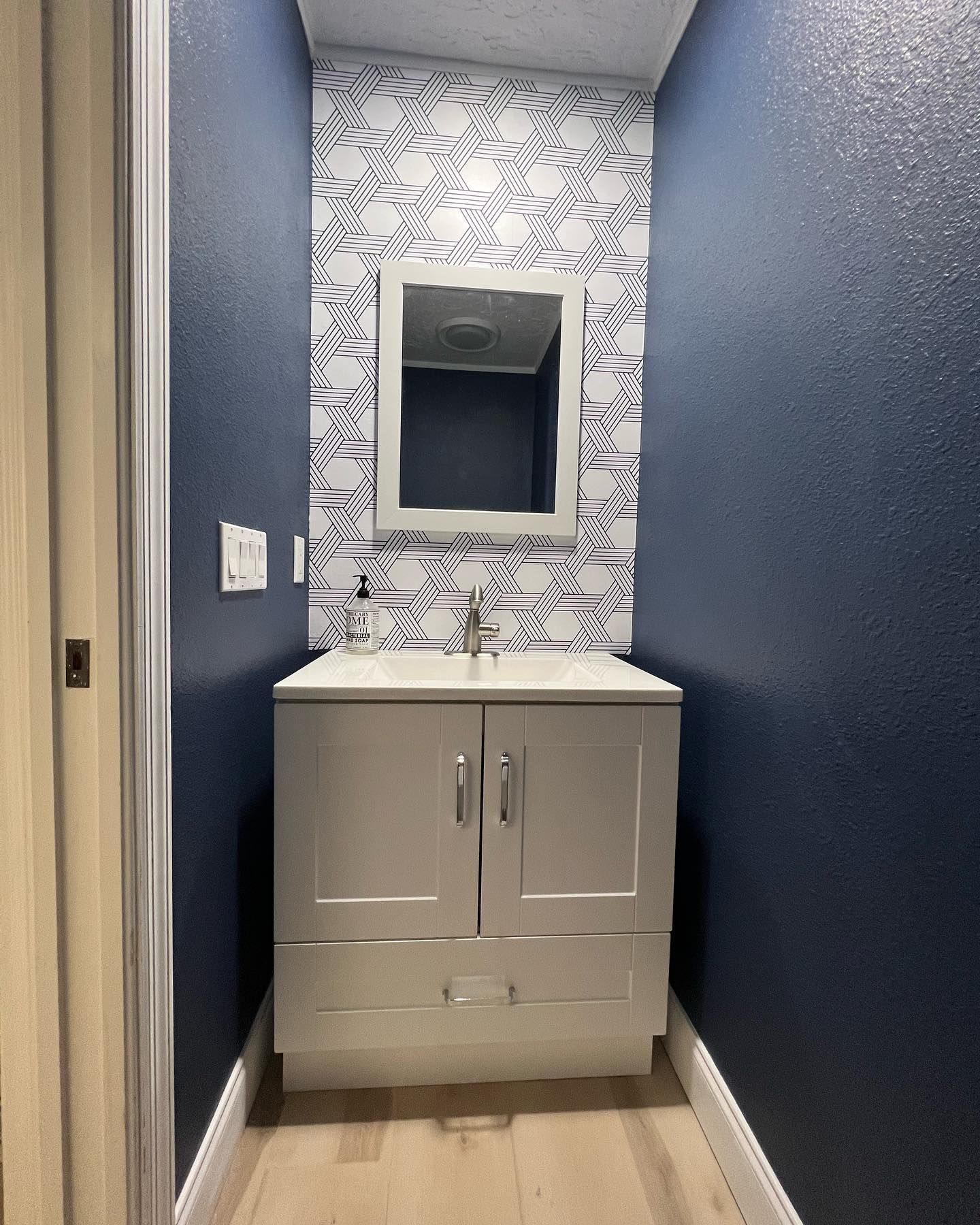 Small, modern bathroom with navy blue walls, patterned accent tile, and a gray vanity.