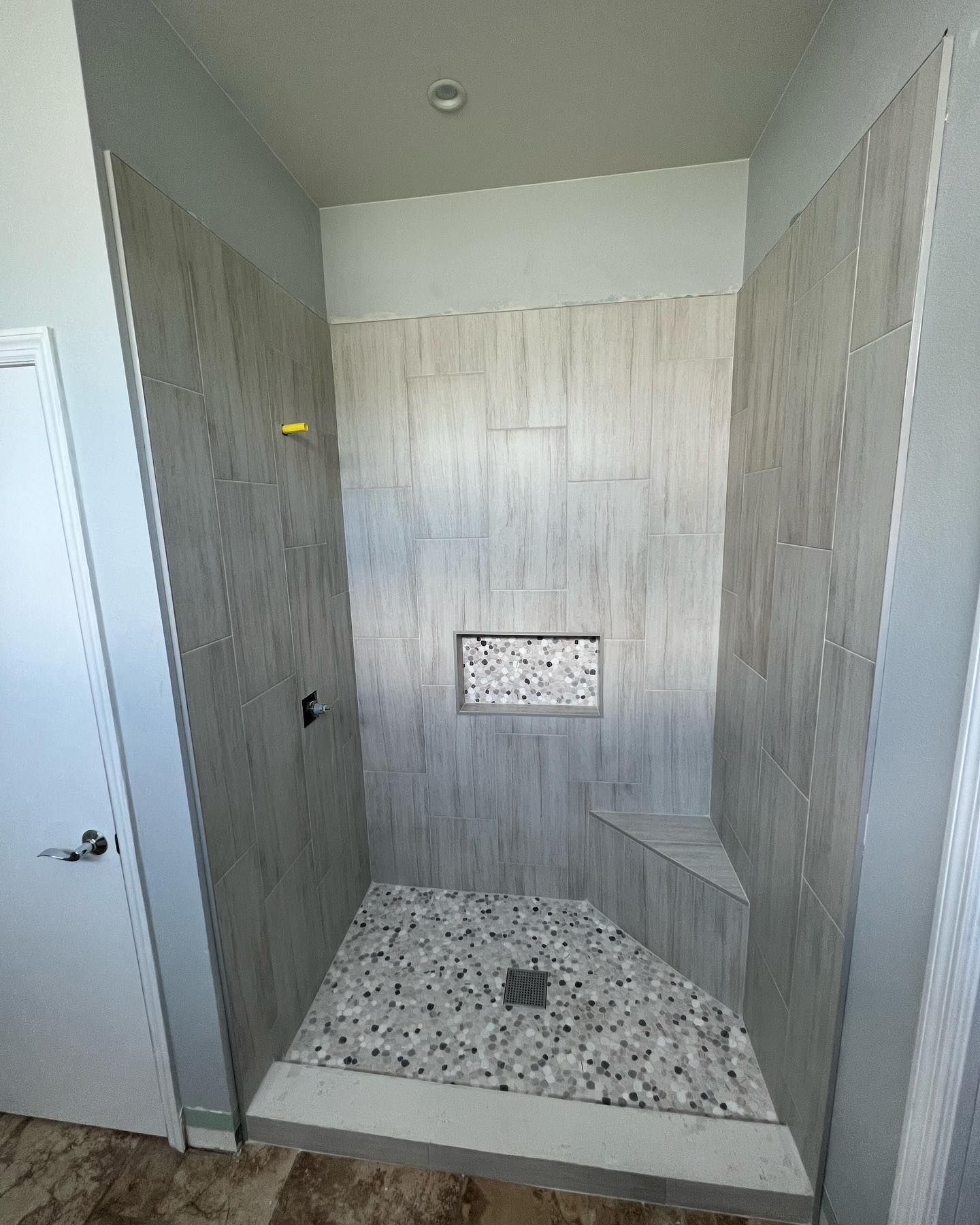 Shower with gray tiled walls, pebble floor, built-in bench, and rectangular storage niche.