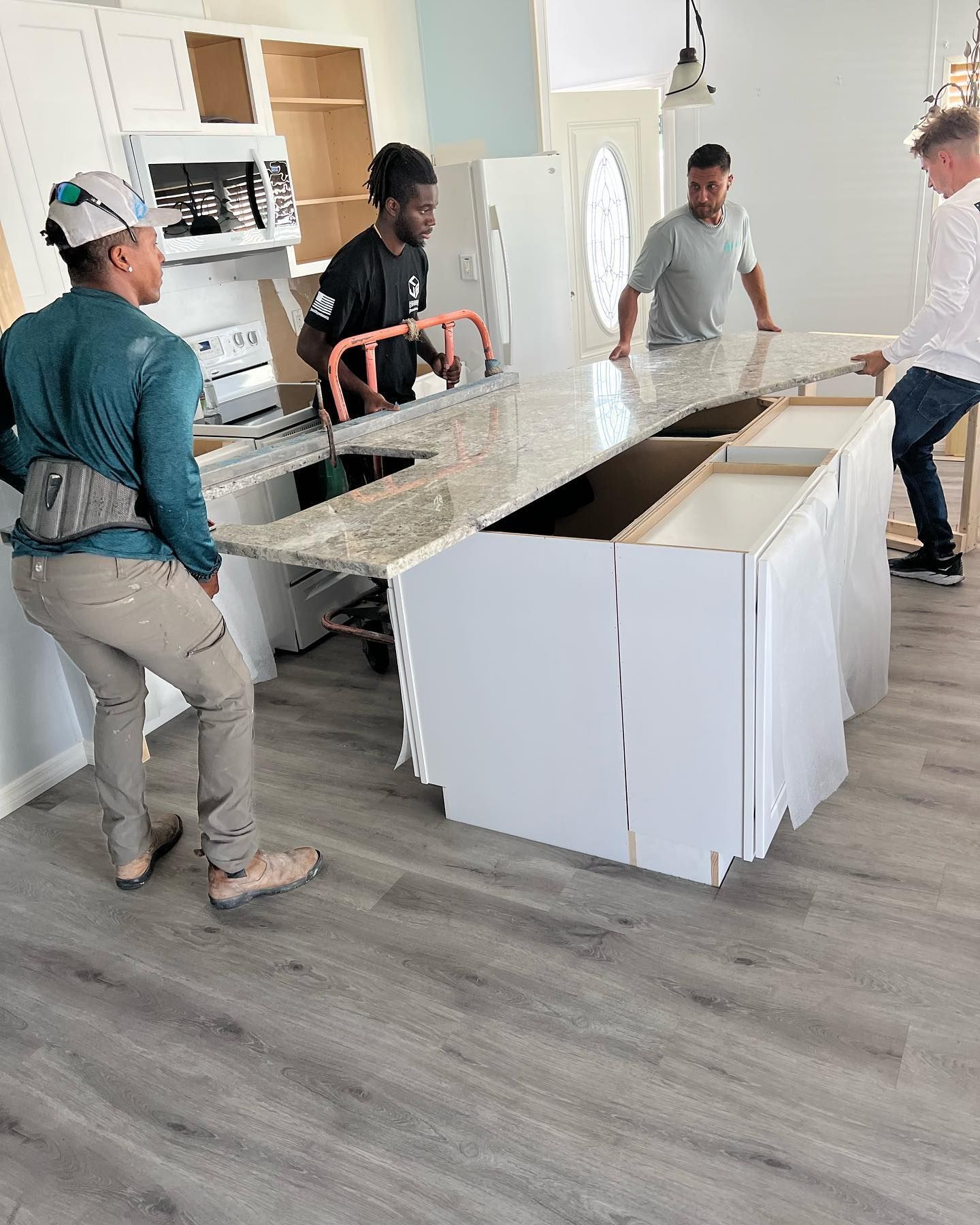 Four people install a white kitchen island countertop in a room with light blue walls and gray flooring.