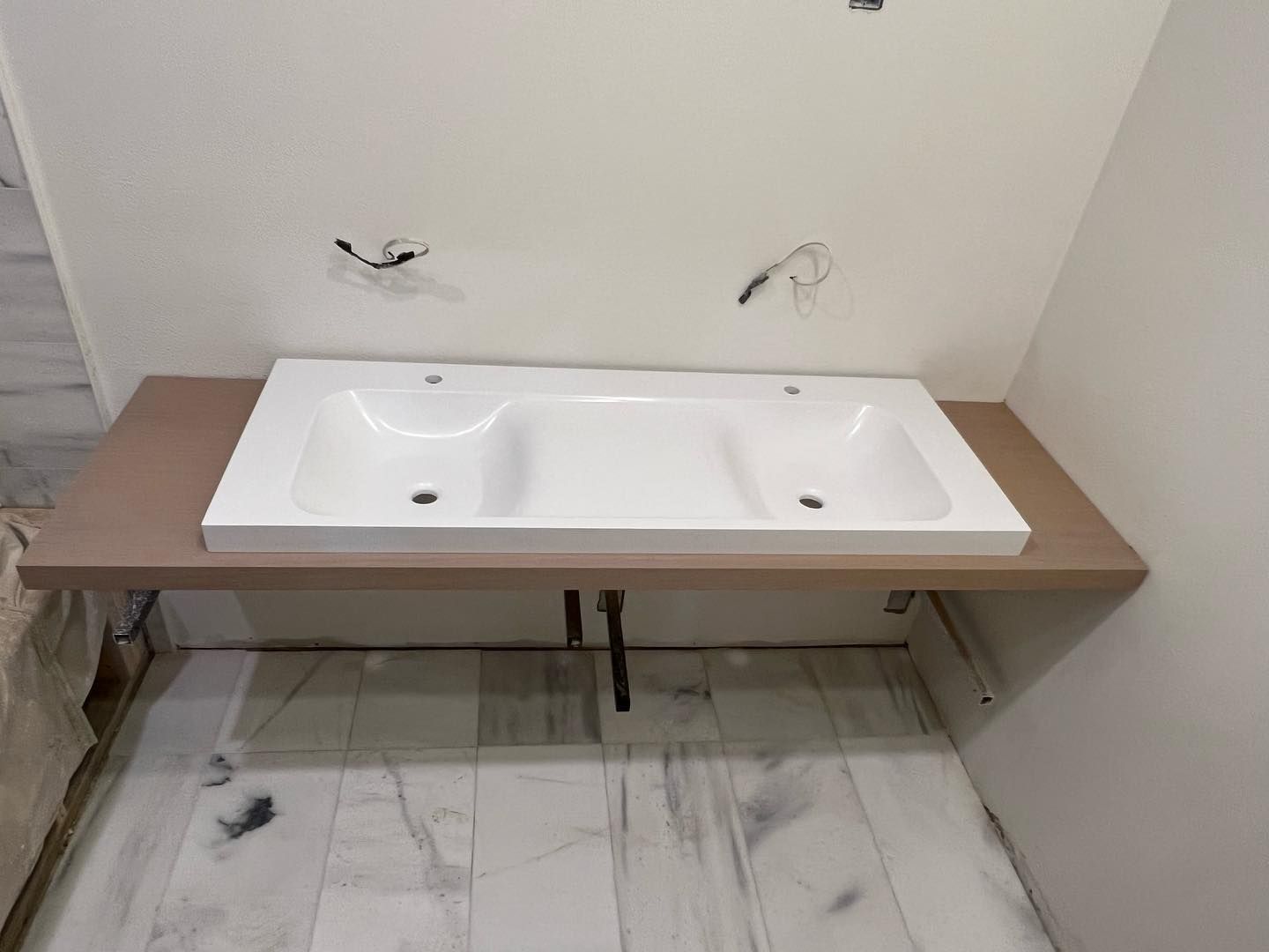 White double sink installed on a wooden shelf in a bathroom under construction.