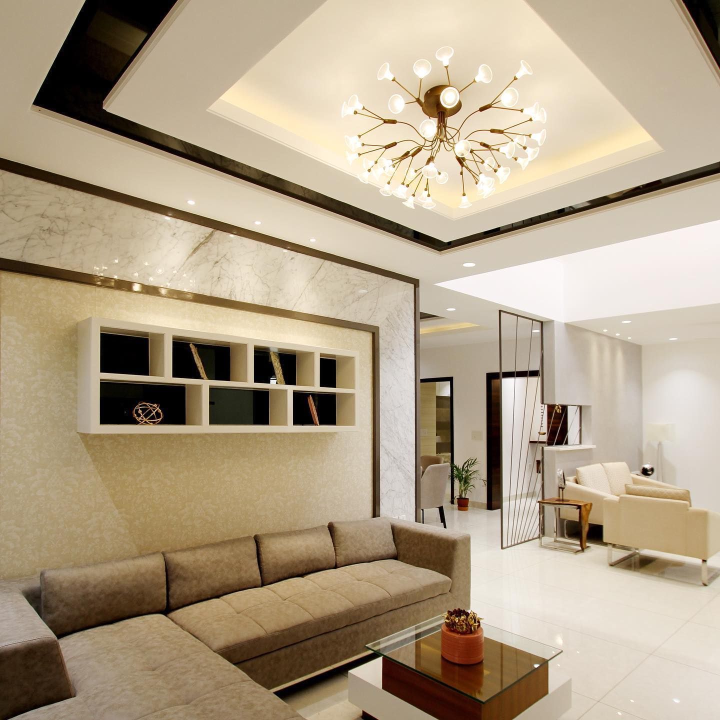 Living room with beige sectional sofa, white shelves, and modern chandelier.