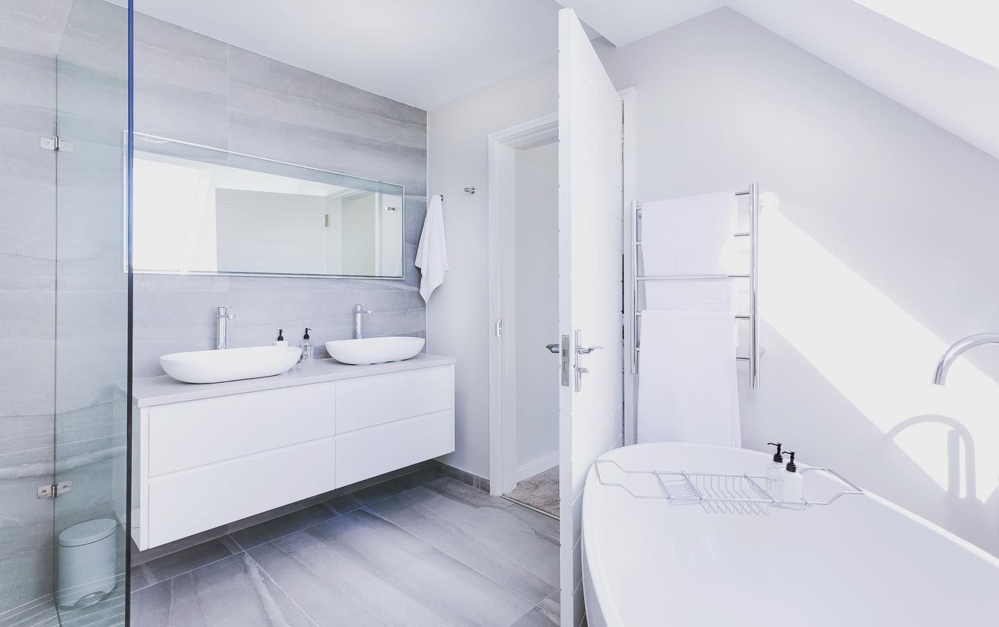Modern white bathroom with double sinks, tub, and glass shower.