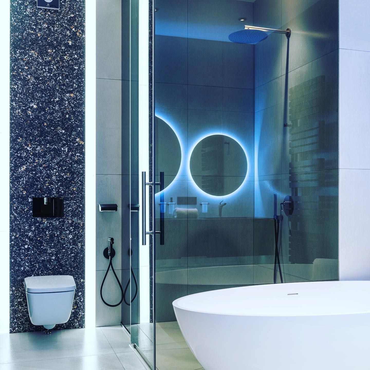 Modern bathroom with blue lighting, glass shower, and a white soaking tub.